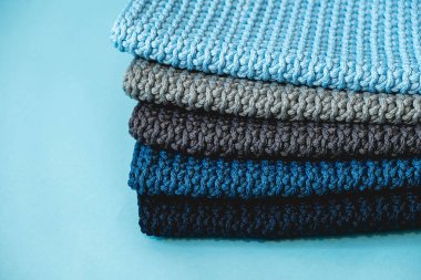 Mavi arka planda koyu mavi, açık mavi ve gri renkli ipliklerden örülmüş bir yığın malzeme. Kopyala, metin için boşluk.
