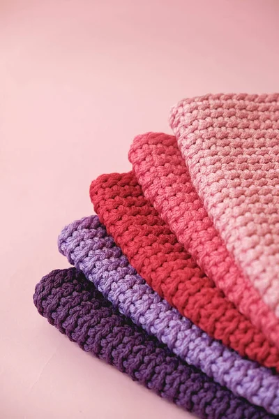 Stack of knitted material from threads of pink, red, purple colors on a pink background. Top view. Copy, empty space for text.