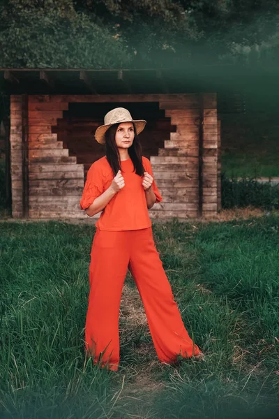 赤い服を着た藁帽子の美しい女性は 木造の家の背景に立っています テキストのコピー 空のスペース — ストック写真