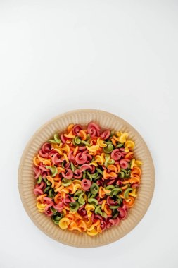 Tek kullanımlık kağıt tabakta beyaz arka planda çok renkli makarna. Üst Manzara. Kopyala, metin için boşluk.