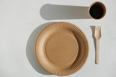 Eko Kraft kağıt sofra takımı. Tek kullanımlık sofra takımı, kraft kağıt tabak ve beyaz arka planda ahşap çatal. Geri dönüşüm konsepti. Sıfır atık.