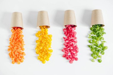 Tek kullanımlık kağıt bardaklarda beyaz arka plana saçılmış çok renkli makarna. Üst Manzara. Kopyala, metin için boşluk.