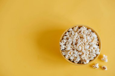 Sarı arka planda sarı bir kasede patlamış mısır. Üst Manzara. Kopyala, metin için boşluk.