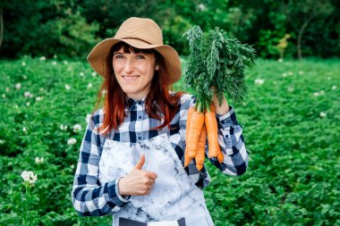 Güzel bir kadın çiftçinin portresi hasır bir şapka içinde bir demet havuç tutuyor ve sebze bahçesindeki bitkilerle çevrili..