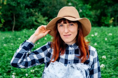 Hasır şapka takmış kameraya gülümseyen güzel bir kadın çiftçi portresi ve sebze bahçesindeki bitkilerle çevrili..