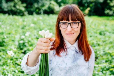 Elinde taze soğan, kameraya gülümseyen ve sebze bahçesinde bir sürü bitkiyle çevrili güzel bir kadın çiftçinin portresi..
