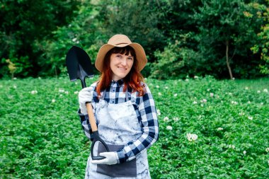 Yeşil tarla ve bahçenin arka planında kürekle hasır şapkalı kadın çiftçi. Metin veya reklam için yer.