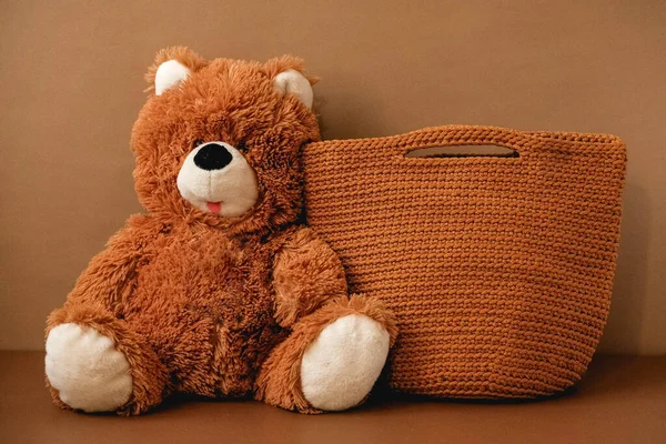 Toy teddy bear with a knitted bag on a brown background. Copy, empty space for text.