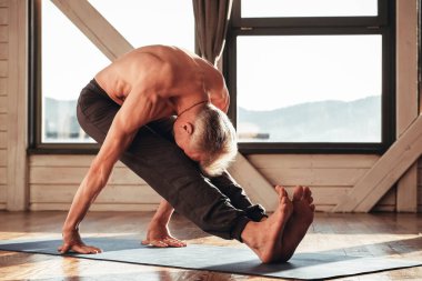 Çıplak gövdeli bir adam stüdyoda pencerenin önünde yoga eğitimi alıyor. Kopyala, metin için boşluk.