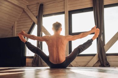 Çıplak gövdesi olan yaşlı bir adam stüdyoda pencerenin önünde yoga yapıyor. Kopyala, metin için boşluk.