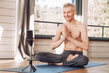 Çıplak gövdeli son sınıf öğrencisi stüdyoda akıllı telefondan yoga dersi alıyor. Kopyala, metin için boşluk.