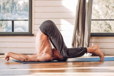 Kafkasyalı son sınıf öğrencisi stüdyoda yoga klasiği yapıyor, pencerenin önünde antrenman yapıyor. Kopyala, metin için boşluk.