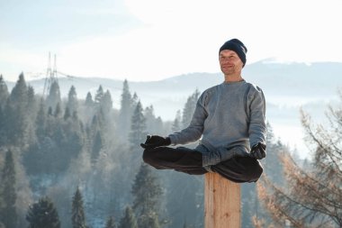 Adam kış dağlarında meditasyon pozisyonunda oturuyor. Kopyala, metin için boşluk.