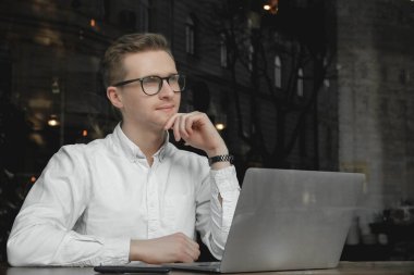 Genç adam beyaz gömlek ve gözlük takıyor dizüstü bilgisayarla oturuyor ve kafede çalışıyor. Serbest meslek kavramı. Kopyala, metin için boşluk.