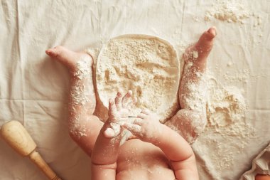 Şef şapkası takmış küçük fırıncı çocuk kahverengi arka planda un ile ahşap bir raptiye, yuvarlak bir süzgeç ve yumurtalarla oynuyor. Üst Manzara. Kopyala, metin için boşluk.