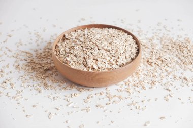 Tahta bir kasede kuru yulaf ezmesi ve beyaz arka planda rastgele dağılmış. Kopyala, metin için boşluk.