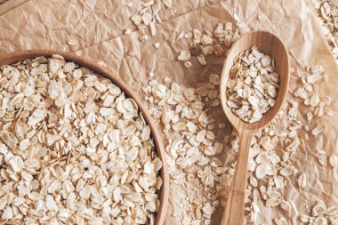 Tahta bir kâsede pişmemiş yulaf ezmesi ve kese kağıdında kaşık. Üst Manzara. Kopyala, metin için boşluk.