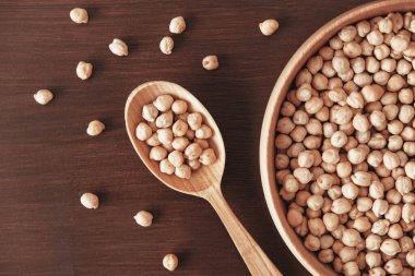 Tahta bir tabakta kuru nohut ve kahverengi ahşap bir arka planda kaşık. Üst Manzara. Kopyala, metin için boşluk.