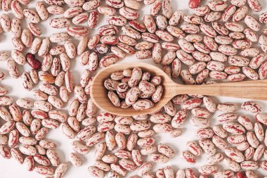 Beyaz arka plana saçılmış tahta kaşıkta çiğ fasulye. Üst Manzara. Kopyala, metin için boşluk.