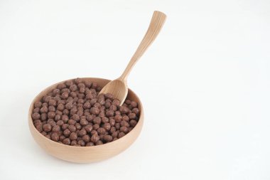 Tahta bir kasede çikolatalı mısır topları ve beyaz bir arka planda kaşık. Kopyala, metin için boşluk.