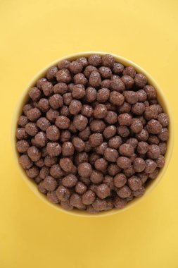 Sarı arka planda sarı bir kasede çikolatalı mısır gevreği topları. Üst Manzara. Kopyala, metin için boşluk.