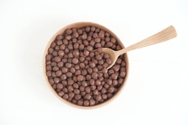 Tahta bir kasede çikolatalı mısır topları ve beyaz bir arka planda kaşık. Üst Manzara. Kopyala, metin için boşluk.