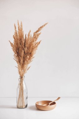 Empty wooden bowl and wooden spoon with dry grass in a bottle on a white table background. Copy, empty space for text.
