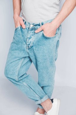 Beyaz arka planda açık renk tişörtlü ve kot pantolonlu bir adam. Kopyala, metin için boşluk.