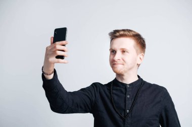 Beyaz bir arka planda elinde akıllı bir telefonla siyah gömlekli genç adam portresi. Kopyala, metin için boşluk.