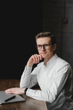 Beyaz tişörtlü ve gözlüklü genç bir adam dizüstü bilgisayarla oturuyor ve kafede çalışıyor. Serbest meslek kavramı. Kopyala, metin için boşluk.