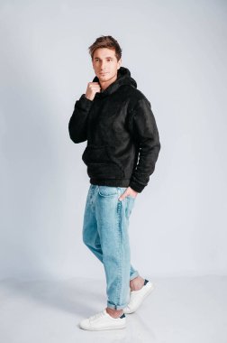 Beyaz arka planda kapüşonlu siyah kazaklı genç bir adam. Kopyala, metin için boşluk.