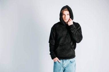 Beyaz arka planda kapüşonlu siyah kazaklı genç bir adamın portresi. Kopyala, metin için boşluk.