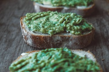 Ahşap zemin üzerinde avokado bulunan çavdar ekmeği dilimleri, basit bir köy sandviçi. Kopyala, metin için boşluk.