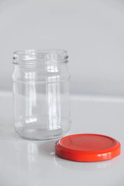 Empty glass jar with red cover on white table background. Copy, empty space for text.