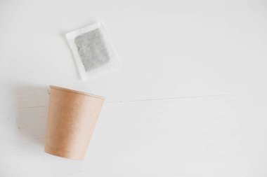 Beyaz arka planda kağıt bardak ve kare şeklinde kuru çay poşeti. Üst Manzara. Kopyala, metin için boşluk.