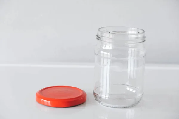 Empty glass jar with red cover on white table background. Copy, empty space for text.