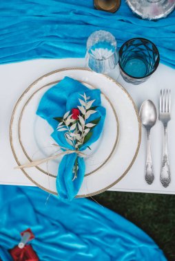 Mavi kumaşla kaplı beyaz ziyafet masası, tabaklar, çatal bıçak takımı, bardaklar, mumlar ve çiçek aranjmanları ile servis ediliyor. Üst Manzara. Kopyala, metin için boşluk .