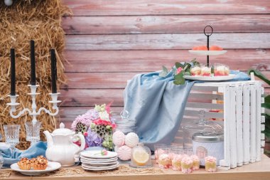 Tabaklar, çatal bıçaklar, bardaklar, mumlar ve çiçek düzenlemeleriyle süslenmiş köy usulü bir tatlı masası. Kopyala, metin için boşluk.