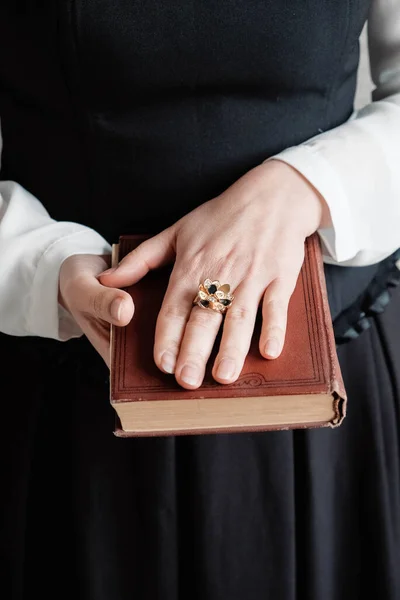 Antique torn book with a hands of a young woman held against black dress. Copy, empty space for text.