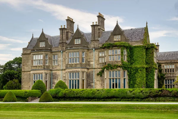 Muckross Evi ve bahçeleri bulutlu gökyüzüne karşı. Killarney Ulusal Parkı 'nda bulunan Tudor tarzında tasarlanmış bir malikanedir..