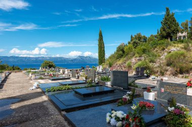 Hırvatistan 'ın Trpanj kenti ve Güney Dalmaçya' daki mezarlıkta, arka planda deniz ve dağlar bulunan mezar taşları ve çiçekler bulunuyor..