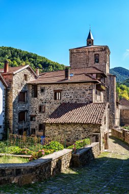 Roncal vadisinde, Pireneler 'de, İspanya' da kahverengi kiremitli konut binaları ve ortaçağ güçlendirilmiş Aziz Kıbrıs kilisesi ile Isaba 'da geziniyor.