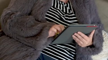 Tavşan kürkü ceketli kadın merkez ofiste tabletle çalışıyor.