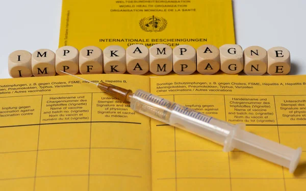 使い捨て注射器とドイツ語の予防接種本と単語予防接種キャンペーン — ストック写真