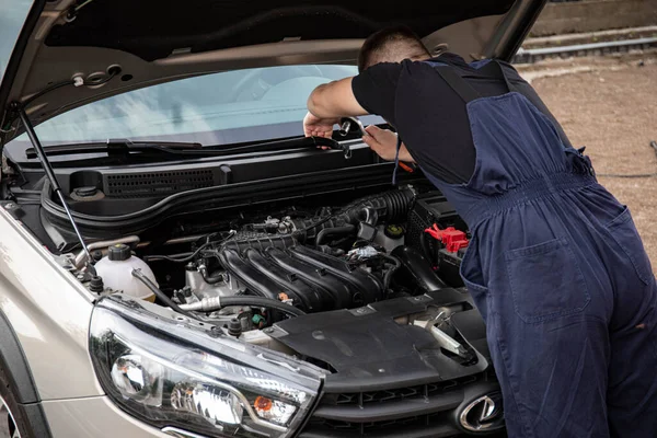 a man repairs a car. a man in blue special clothes to repair the car. engine parts machine repair maintenance breakage problem hands people man master