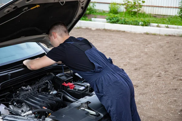 a man repairs a car. a man in blue special clothes to repair the car. engine parts machine repair maintenance breakage problem hands people man master