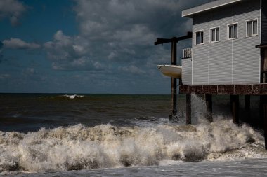 Deniz dalgaları fırtınada evi dövüyor. Siyah deniz mavi gökyüzü dalgalı deniz fırtınası