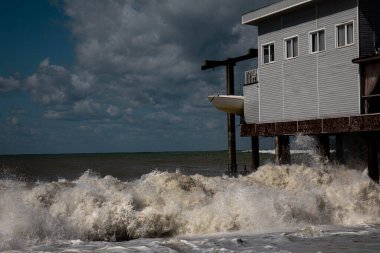 Deniz dalgaları fırtınada evi dövüyor. Siyah deniz mavi gökyüzü dalgalı deniz fırtınası
