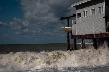 Deniz dalgaları fırtınada evi dövüyor. Siyah deniz mavi gökyüzü dalgalı deniz fırtınası
