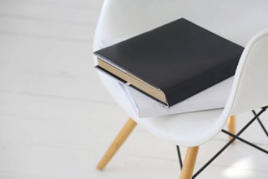 Siyah beyaz kitapları olan beyaz rahat bir sandalye. Gün ışığı ışığı. Beyaz ahşap arka plan. Minimalizm tarzı. Uzayı sola kopyala
